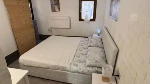 Une chambre à coucher avec un lit, une porte en bois, une fenêtre et un climatiseur fixé au mur.