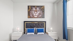 Een moderne slaapkamer met een gestoffeerd hoofdeinde, een groot kunstwerk van een tijger aan de muur, en een bed met blauw-witte kussens.