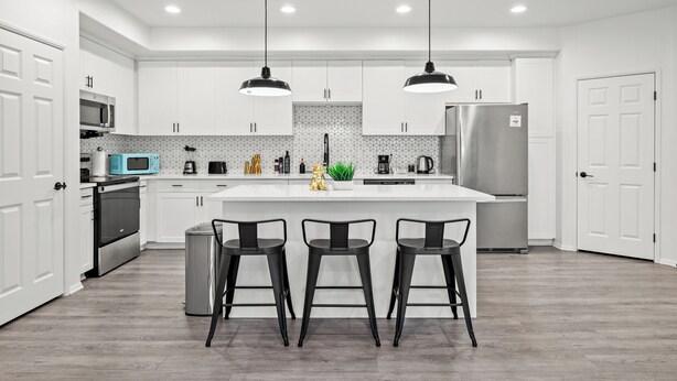 Een moderne keuken met witte kastjes, een centraal eiland met barstoelen, roestvrijstalen apparatuur en hanglampen.