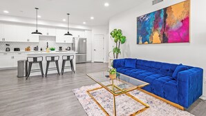 Een moderne woonkamer met een blauwe bank, een glazen salontafel en een kleurrijk abstract schilderij aan de muur.