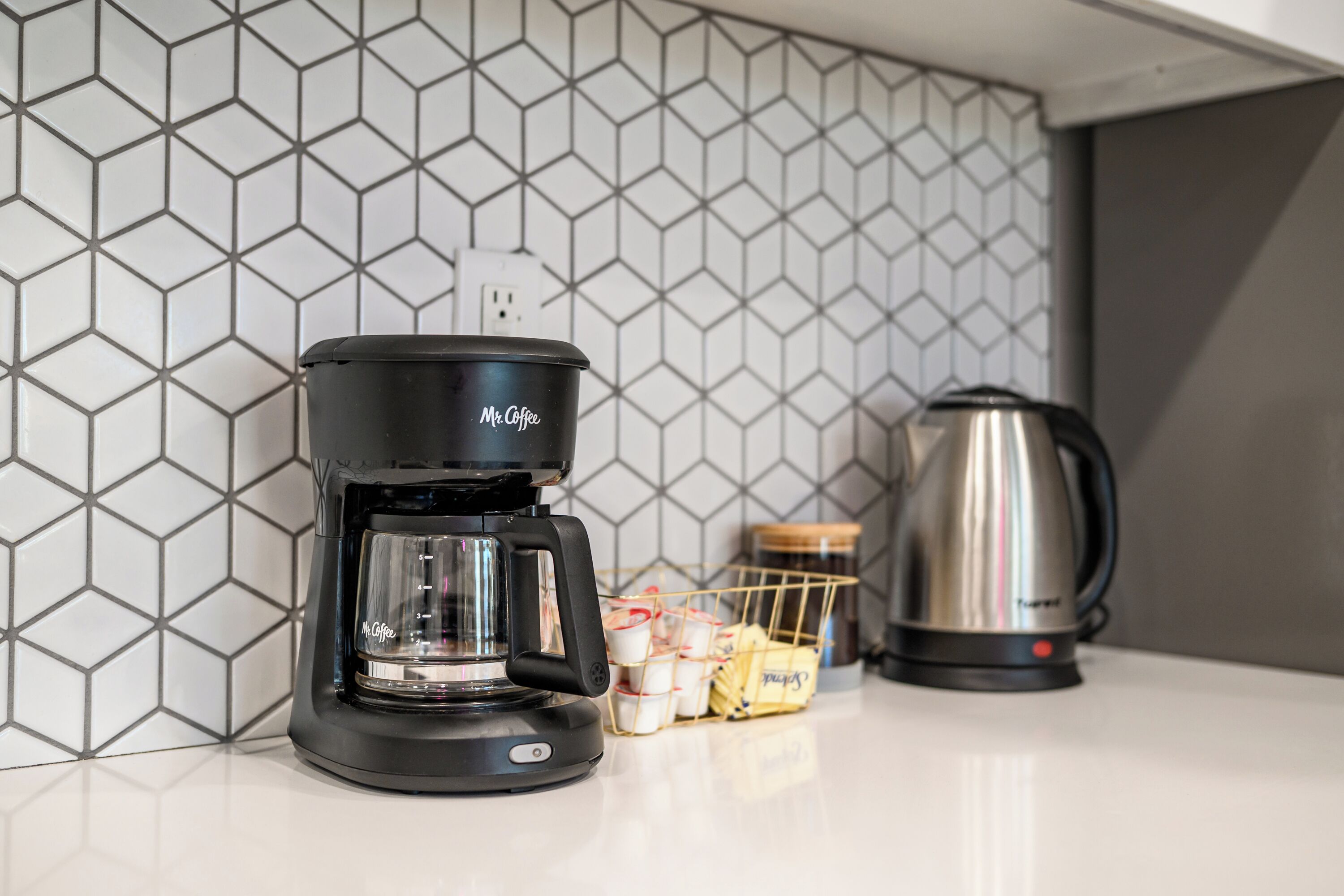 A coffee maker, a kettle, and a basket of coffee pods on a countertop.