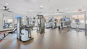 Een sportschool met diverse fitnessapparaten, spiegels en een plafondventilator.