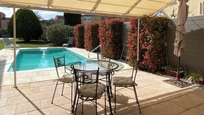 Ett takförsett utomhusområde med en pool, ett bord med stolar och en vägg full av blommande växter.
