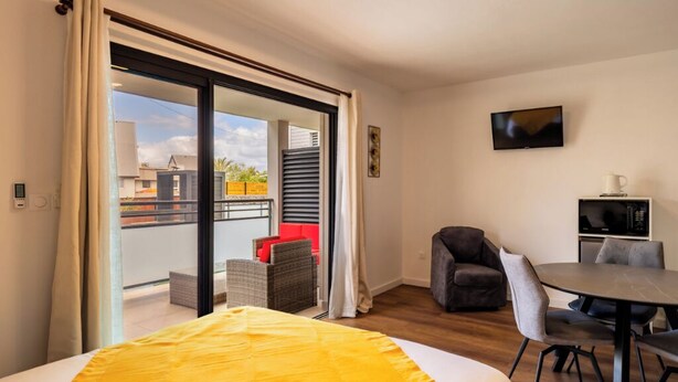 Ein Hotelzimmer mit Bett, Esstisch, Fernseher und Balkon mit einem roten Stuhl.
