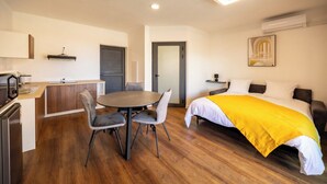 Ein kleines Hotelzimmer mit Bett, Esstisch mit Stühlen, einer Küchenzeile und einer Tür zu einem weiteren Raum.