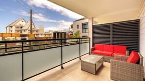 Ein Balkon mit rotem Sofa, Korbmöbeln und Blick auf umliegende Gebäude.