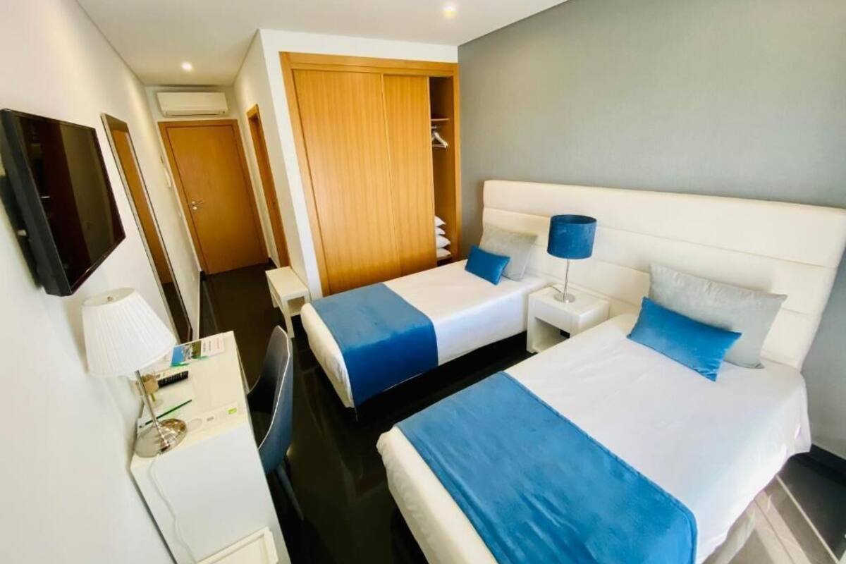 Une chambre d’hôtel avec deux lits, un bureau, une chaise, une télévision et une armoire.