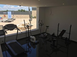 Gimnasio con equipo de ejercicio, cinta de correr y vistas a la zona de la piscina.