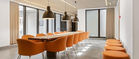 Una sala de conferencias moderna con una larga mesa, sillas color naranja e iluminación colgante.