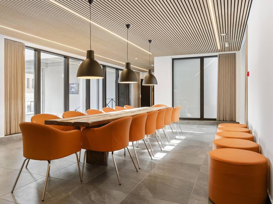 A modern conference room with a long table, orange chairs, and pendant lighting.