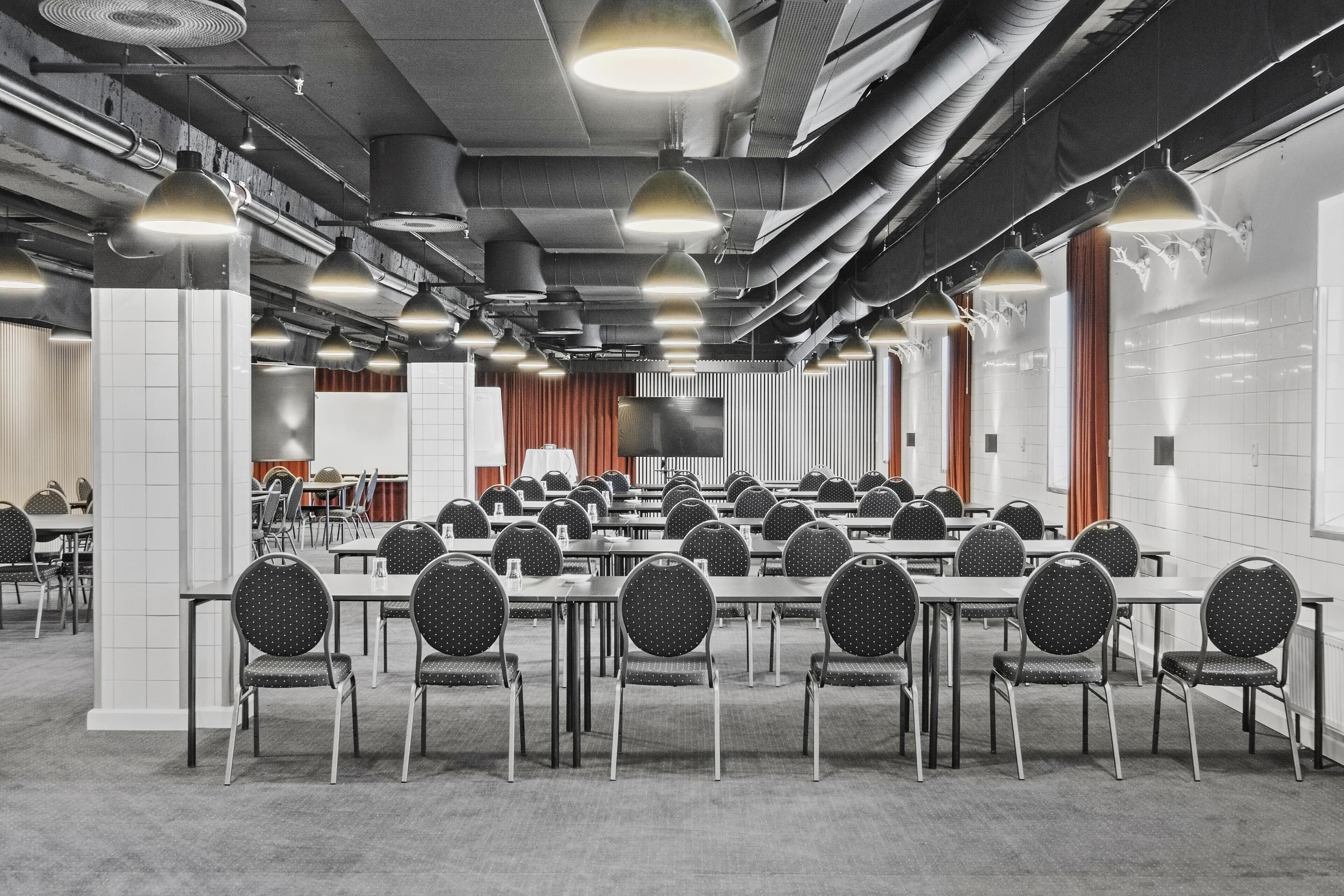 A conference room with tables and chairs, overhead lighting, and visible ductwork.