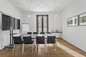 Uma sala de conferência com uma grande mesa, cadeiras pretas, um quadro branco e uma tela de TV.