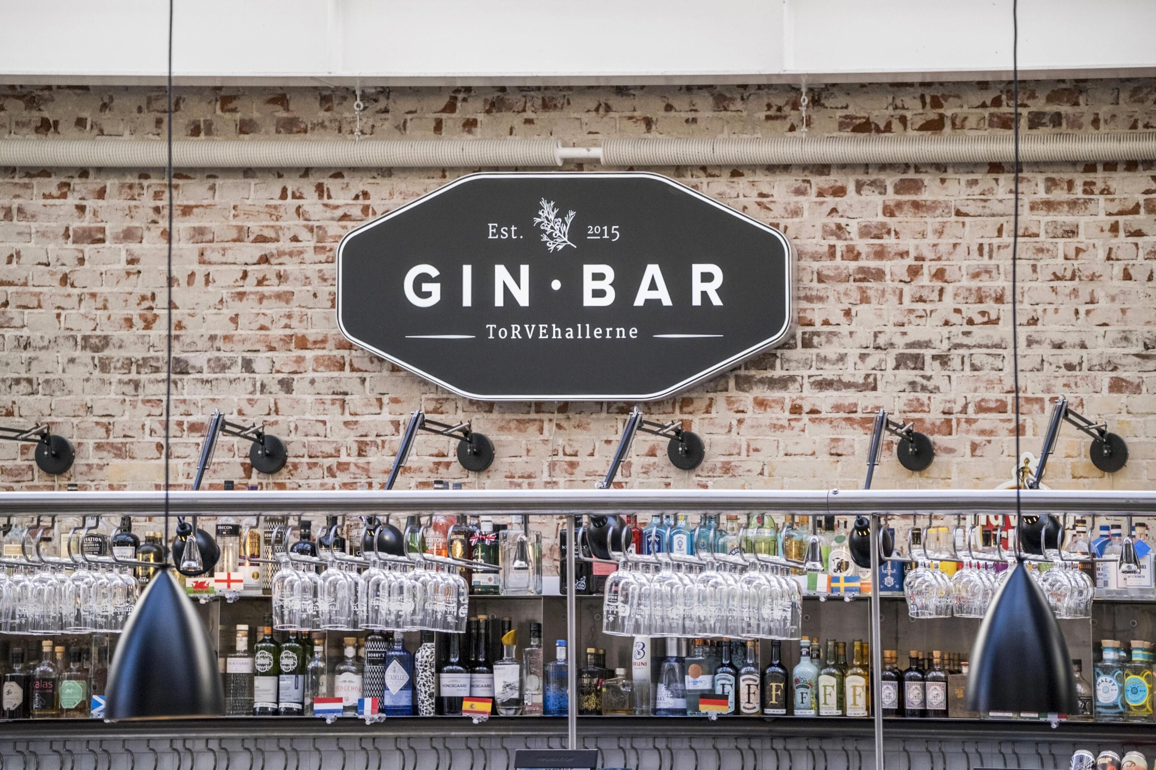 A bar with a sign reading 'GIN BAR' and a brick wall background.