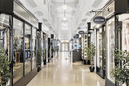 A corridor with glass-fronted shops, including a jewelry store and a hotel.. Villavejle Hotel, BW Signature Collection