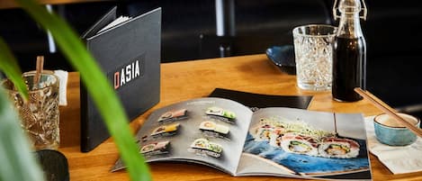 A menu with various food items, a bottle, and a glass on a wooden table.