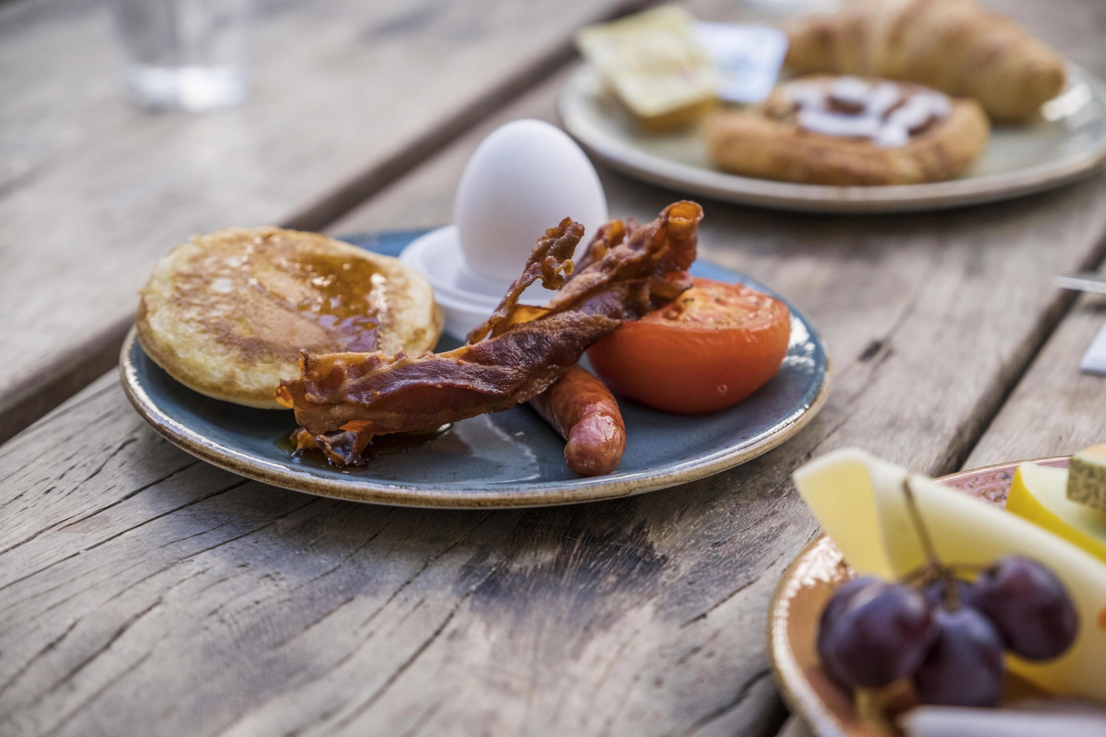 A breakfast plate with pancakes, bacon, a tomato, and a boiled egg.