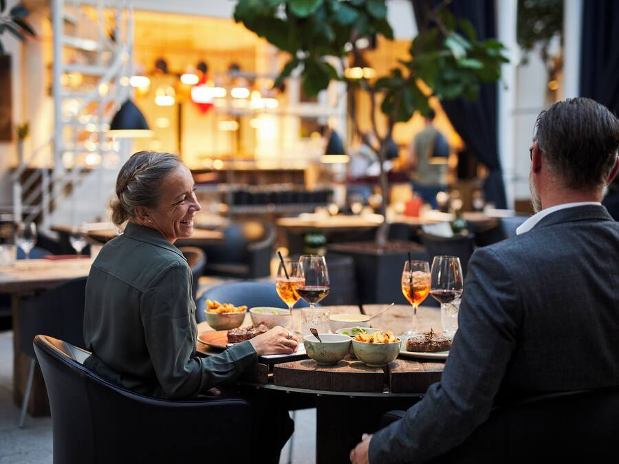 Two people dining at an outdoor restaurant with tables, chairs, and a warm ambiance.