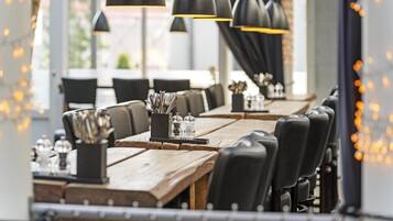Interior de restaurante con mesas de madera, sillas negras e iluminación colgante.