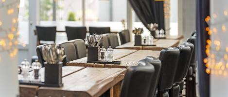 Interior de restaurante con mesas de madera, sillas negras e iluminación colgante.