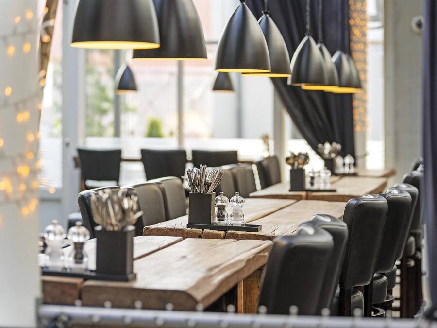 Interior de restaurante con mesas de madera, sillas negras e iluminación colgante.