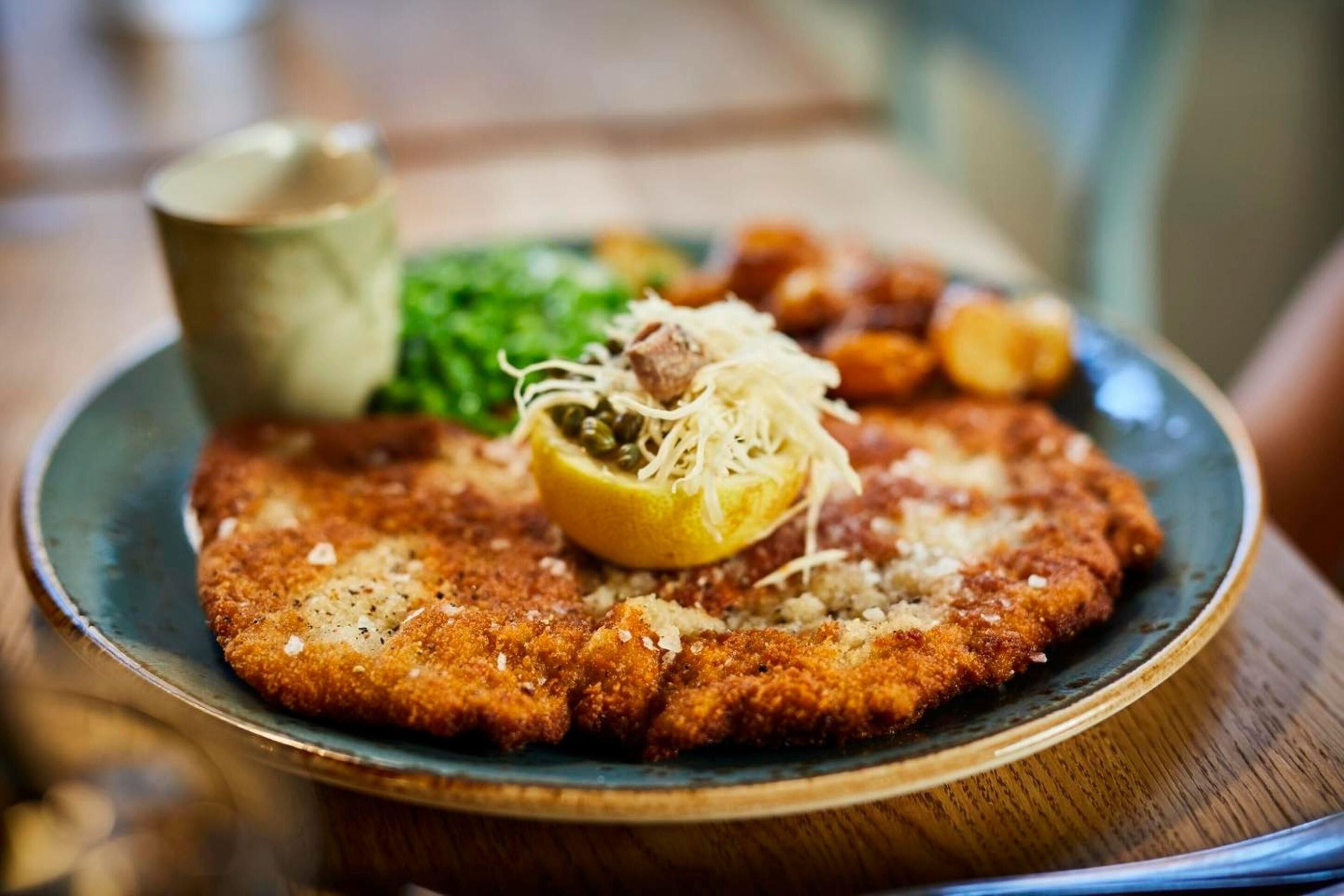A plate with a breaded cutlet, a lemon wedge, and a small cup of sauce.