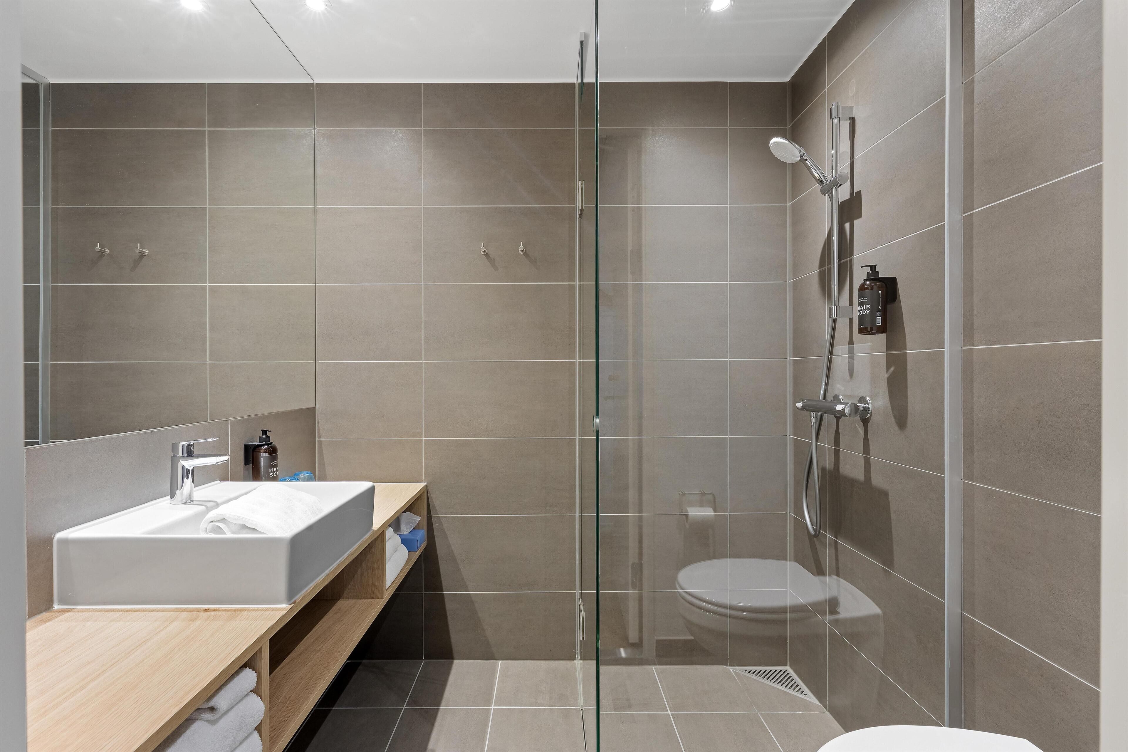 Une salle de bain moderne avec une douche à parois de verre, un lavabo avec un miroir et des toilettes.