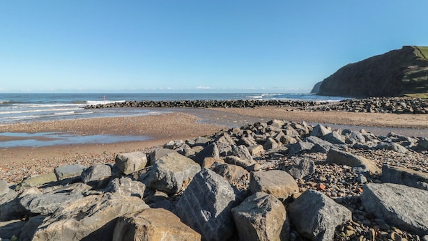 A rocky beach with a clear sky and distant mountains.