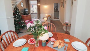 A dining area with a wooden table set for two, a Christmas tree, and a vase with flowers.