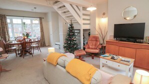 A living room with a sofa, ottoman, coffee table, TV, and a Christmas tree.