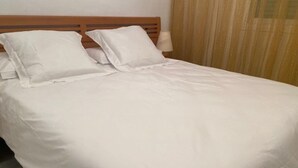 Un lit bien fait, avec du linge de lit blanc et une tête de lit en bois.