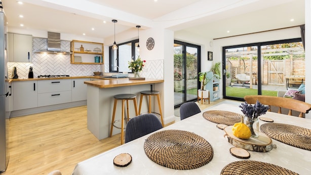 A modern kitchen with a central island, bar stools, and a dining area with a table set for two. - Family Friendly 3 Bed Home - Pass the Keys (Leamington Spa)