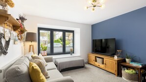 A modern living room with a grey sofa, a wooden TV stand, and a large window. - Family Friendly 3 Bed Home - Pass the Keys (Leamington Spa)