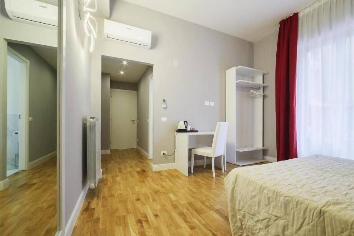 Hotellihuone, jossa on sänky, työpöytä, tuoli, vaatekaappi ja ilmastointilaite.