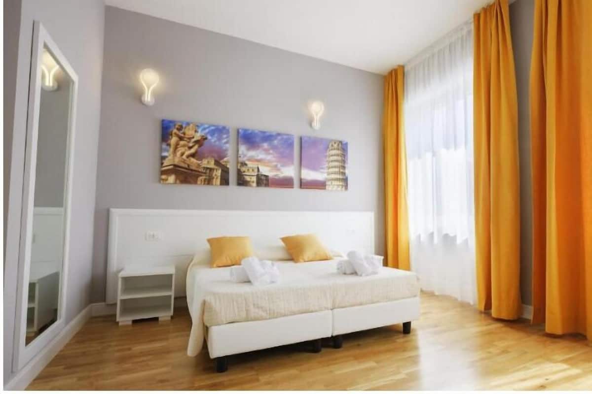 Hotellihuone, jossa on sänky, yöpöytä ja kolme taulua seinällä.