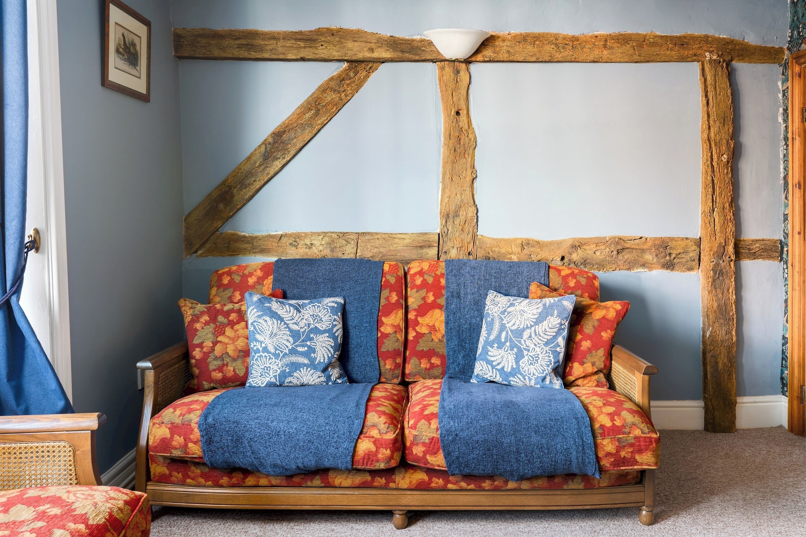 Ein traditionell eingerichteter Raum mit freiliegenden Holzbalken, einer Couch mit gemusterten Kissen und einem blauen Vorhang.