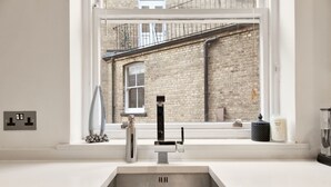 Een moderne keuken met een roestvrijstalen spoelbak, een raam met uitzicht op een bakstenen gebouw en een klein vensterbankje met decoratieve objecten.