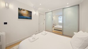 Een moderne hotelkamer met een groot bed, een inloopkast met glazen schuifdeuren, een schilderij aan de muur en een raam voor natuurlijk licht.