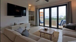Un salon moderne doté d’un téléviseur à écran plat, d’un canapé, d’une table basse et d’une porte-fenêtre coulissante donnant sur un balcon.