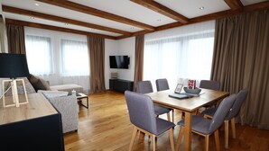 A modern living room with a wooden ceiling, a flat-screen TV, a dining table with chairs, a sofa, and a coffee table. - Apartment Near the Kitzski Area (Jochberg)