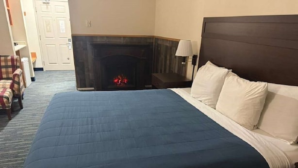 Quarto de hotel com cama grande, lareira, mesa de cabeceira e uma cadeira.