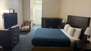 Quarto de hotel com cama, televisão, lareira, cadeira e secretária.