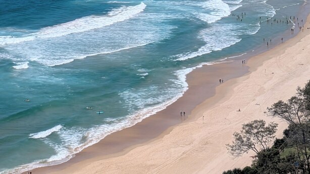 A coastal beach with waves, a sandy shore, and a distant city skyline. - Spacious 4-bedroom apartment in brilliant Surfers Paradise with AC (Surfers Paradise)