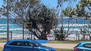 A coastal area with a blue car parked near a beach, a playground, and a view of the ocean. - Spacious 4-bedroom apartment in brilliant Surfers Paradise with AC (Surfers Paradise)