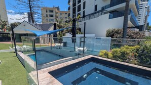 A modern outdoor swimming pool with glass railings and seating, surrounded by well-maintained grass and plants. - Spacious 4-bedroom apartment in brilliant Surfers Paradise with AC (Surfers Paradise)