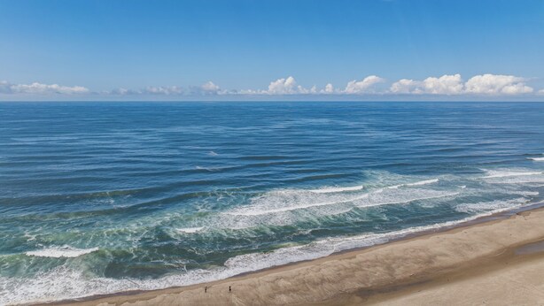 Une plage avec des vagues, un ciel dégagé et des nuages à l’horizon.