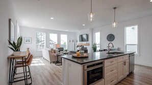Une cuisine moderne dotée d’un îlot central, de planchers en bois et de luminaires suspendus.