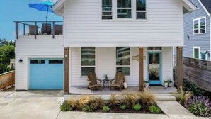 Une maison à deux étages avec un garage, un balcon et une véranda à l’avant, équipée de chaises.