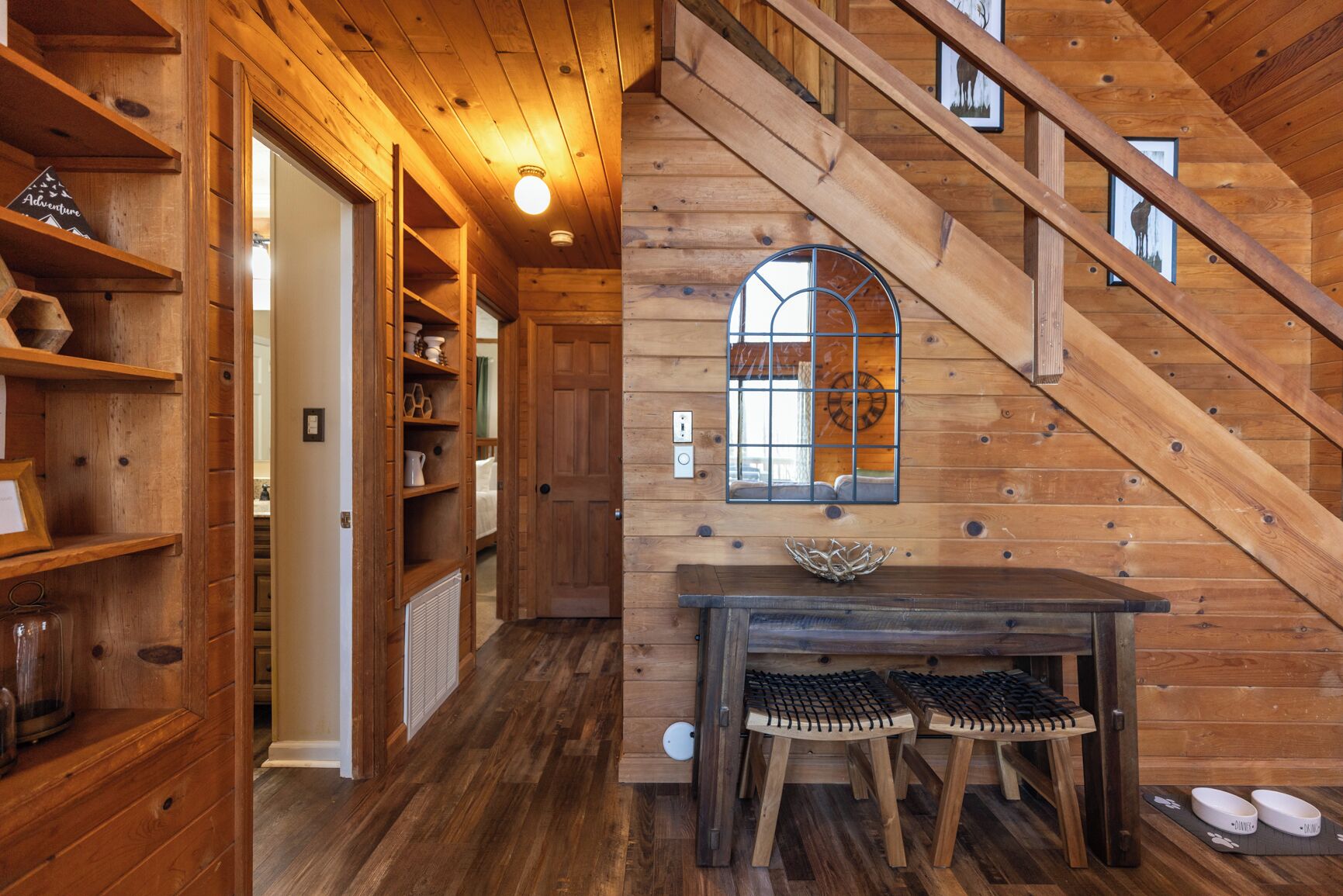 A wooden interior with a staircase, a table with stools, and a decorative window.