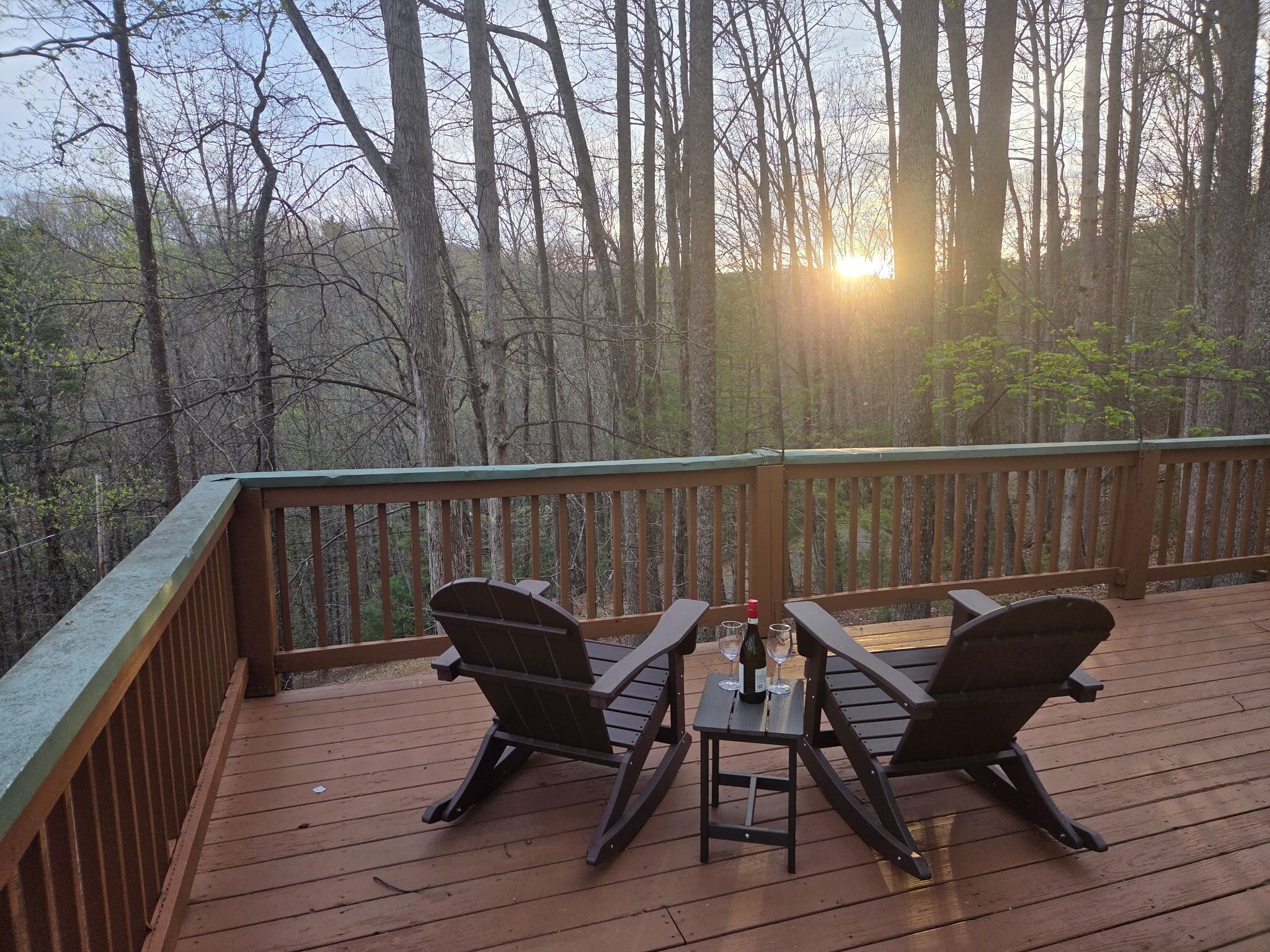 A wooden deck with two chairs and a table, a bottle of wine, and a glass on the table.