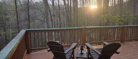 A wooden deck with two chairs and a table, a bottle of wine, and a glass on the table.